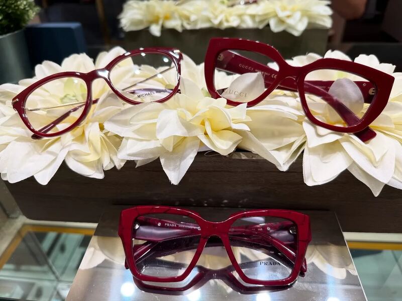 Red Michael Kors, Gucci, and Prada frames arranged on white floral displays