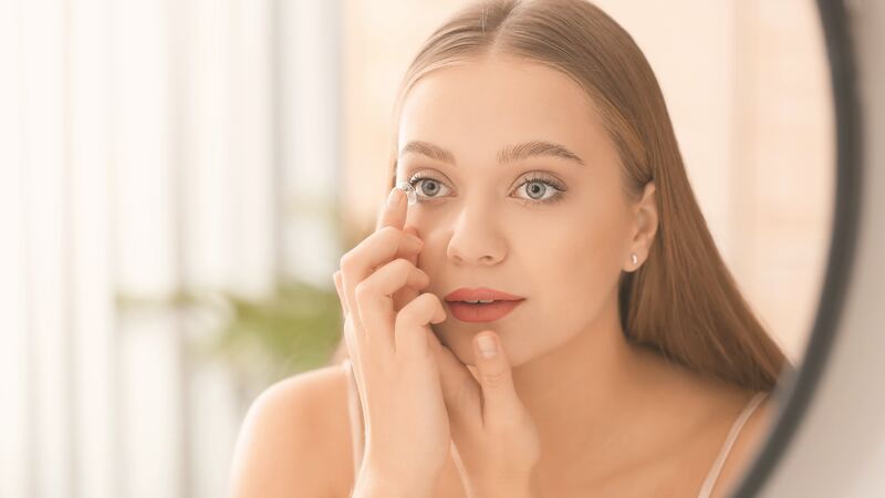 Woman inserting a contact lens while looking in a mirror